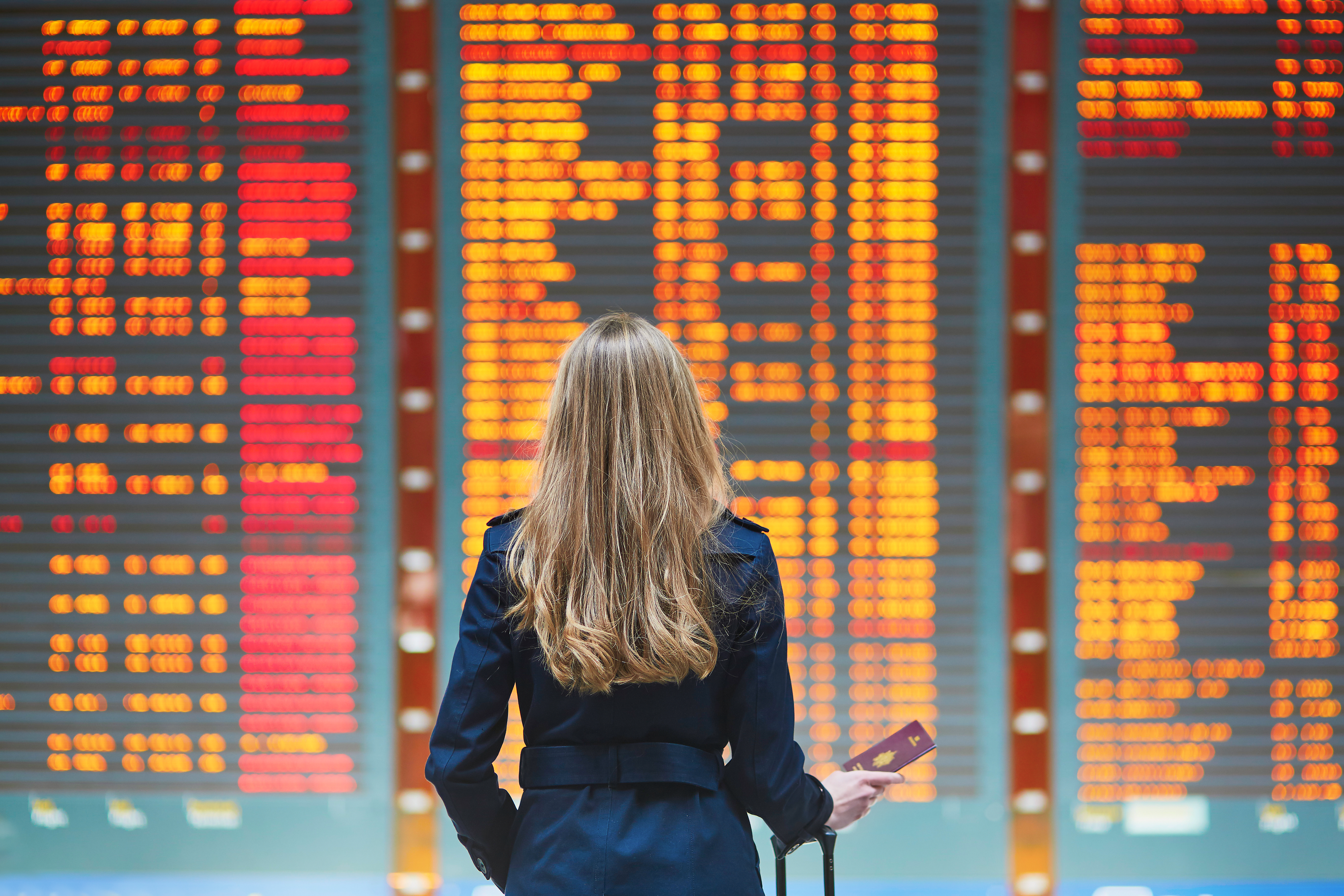 Mujer viajando por negocios frente a pantalla de vuelos en aeropuerto 